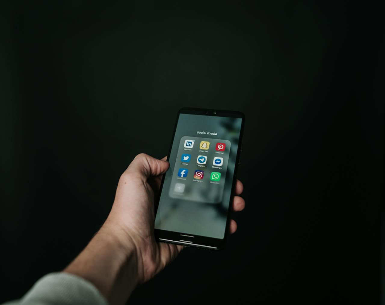 Mastering the First Impression: Your intriguing post title goes here Close-up of a hand holding a smartphone displaying various social media app icons on a dark background.